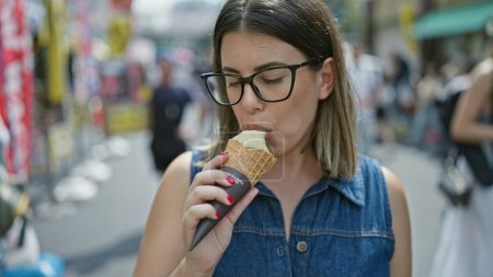 Fröhliche und schöne hispanische Frau in Gläsern genießt fröhlich eine leckere Eistüte inmitten des geschäftigen Tsukiji-Marktes - Tokyo Sommerspaß!