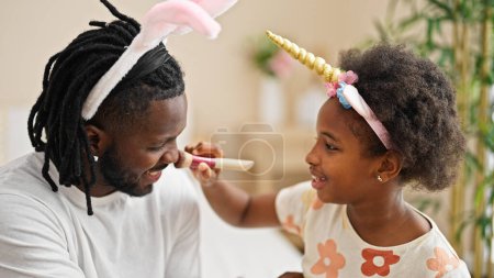 Foto de Afro-americanos padre e hija usando divertido diadema aplicando maquillaje sonriendo en el dormitorio - Imagen libre de derechos