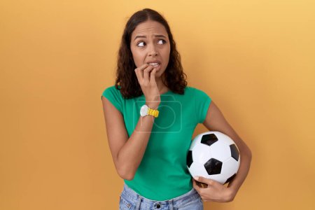 Photo for Young hispanic woman holding ball looking stressed and nervous with hands on mouth biting nails. anxiety problem. - Royalty Free Image