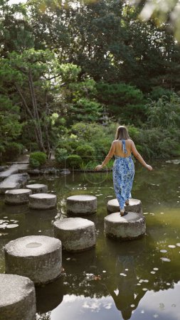 Beautiful hispanic woman's leisurely summer walk along stone path crossing a lake at traditional heian jingu shrine, kyoto