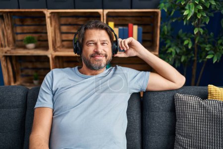 Téléchargez les photos : Moyen Age homme écouter de la musique assis sur le canapé à la maison - en image libre de droit
