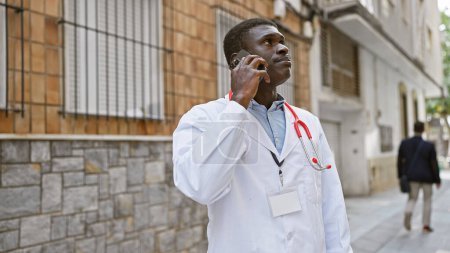 Téléchargez les photos : Médecin afro-américain vêtu d'un manteau blanc lors d'un appel devant un hôpital de la ville. - en image libre de droit