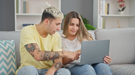 Téléchargez les photos : Beau couple utilisant un ordinateur portable assis sur un canapé souriant à la maison - en image libre de droit