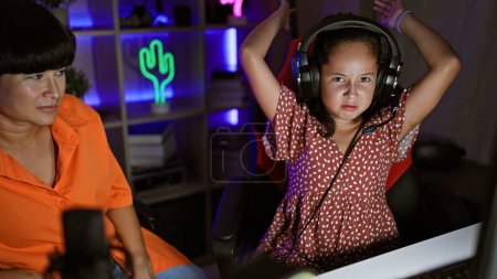 Téléchargez les photos : Duo streamer mère-fille souligné tout en streaming jeu vidéo dans la salle de jeu, mettant en valeur une nuit de jeu en famille allé mal - en image libre de droit