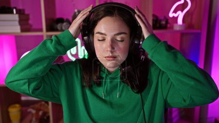 Téléchargez les photos : Une jeune femme portant un casque jouit de la musique dans une salle de jeux vibramment éclairée la nuit - en image libre de droit