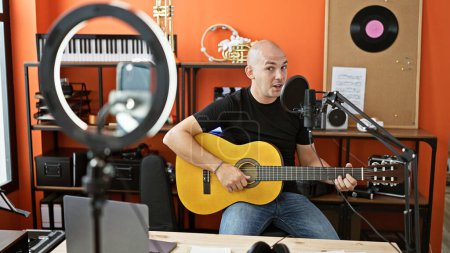 Foto de Joven músico hispano grabando video cantando canción tocando guitarra clásica en estudio de música - Imagen libre de derechos
