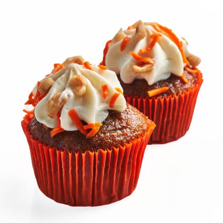 Foto de Dos cupcakes con glaseado cremoso y salpicaduras de naranja aisladas sobre un fondo blanco. - Imagen libre de derechos