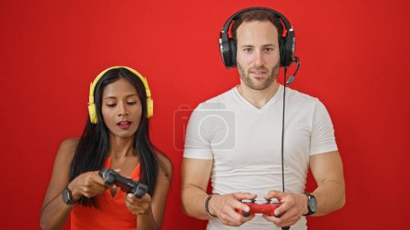Foto de Hermosa pareja sonriendo confiado jugando videojuego sobre fondo rojo aislado - Imagen libre de derechos