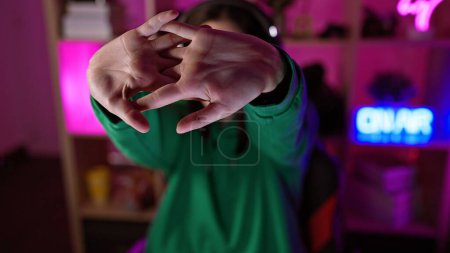 Photo for A young woman gestures with her hands in a dimly lit gaming room with neon lights. - Royalty Free Image