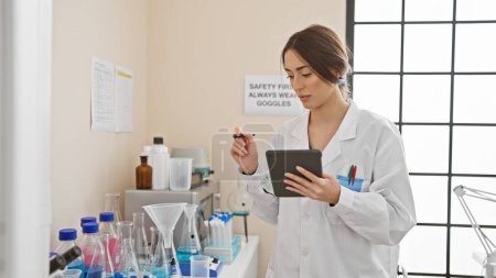 Foto de Una mujer científica enfocada analiza muestras y registra datos en una tableta en un entorno de laboratorio. - Imagen libre de derechos