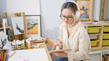 Téléchargez les photos : Jeune artiste blonde dessinant sur papier écoutant de la musique au studio d'art - en image libre de droit