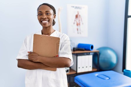 Foto de African american woman physiotherapist smiling confident holding medical report at rehab clinic - Imagen libre de derechos
