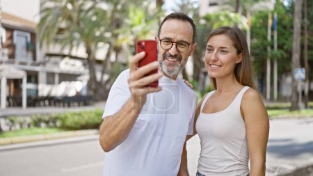 Selbstbewusster Vater und Tochter teilen einen schönen Moment und machen freudig ein cooles Selfie mit ihrem Handy, das auf einer belebten Straße in der Stadt steht.