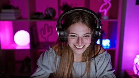 Téléchargez les photos : Une jeune femme souriante avec écouteurs aime jouer dans une chambre vibrante éclairée par le violet la nuit. - en image libre de droit