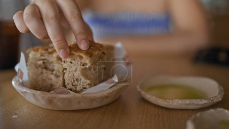 Photo for Young hispanic woman dipping bread into olive oil at the restaurant - Royalty Free Image