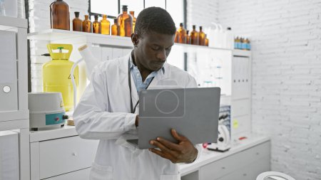 Photo for An african american man in a lab coat analyzing data on a laptop in a modern laboratory setting. - Royalty Free Image
