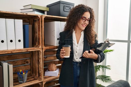 Photo for Young beautiful hispanic woman business worker drinking coffee reading document at office - Royalty Free Image
