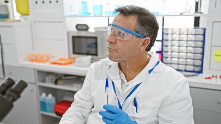 Foto de Un hombre de mediana edad en un laboratorio con gafas de seguridad sosteniendo una pluma, lo que refleja profesionalidad en un entorno de atención médica. - Imagen libre de derechos