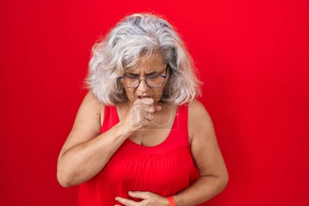 Photo for Middle age woman with grey hair standing over red background feeling unwell and coughing as symptom for cold or bronchitis. health care concept. - Royalty Free Image