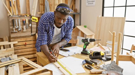 Foto de Un hombre negro experto mide la madera en un taller de carpintería organizado, mostrando artesanía y precisión. - Imagen libre de derechos