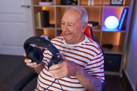 Photo for Middle age grey-haired man streamer smiling confident holding headphones at gaming room - Royalty Free Image