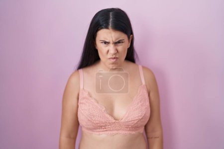 Foto de Mujer hispana joven con sujetador rosa escéptico y nervioso, frunciendo el ceño molesto debido a un problema. persona negativa. - Imagen libre de derechos
