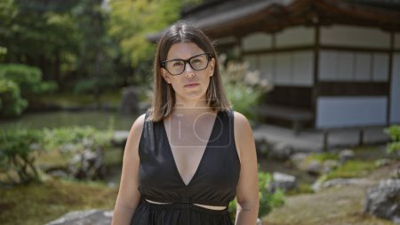 Nachdenkliche und schöne hispanische Frau mit Brille, die widerstandsfähig am Ginkaku-ji-Tempel in Kyoto steht; ein Porträt des Zen inmitten des japanischen Zenit-Gartens