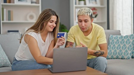 Téléchargez les photos : Magnifiques achats en couple avec ordinateur portable et carte de crédit assis sur le canapé à la maison - en image libre de droit
