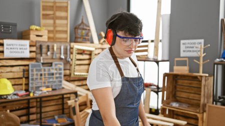 Photo for A young man wearing safety gear works diligently in a well-organized carpentry workshop. - Royalty Free Image