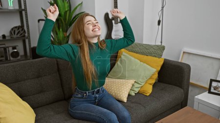 Foto de Una joven alegre que se estira con una amplia sonrisa en un acogedor apartamento moderno sala de estar - Imagen libre de derechos
