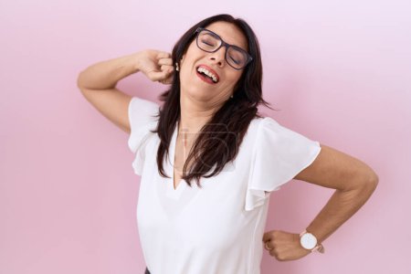 Photo for Middle age hispanic woman wearing casual white t shirt and glasses stretching back, tired and relaxed, sleepy and yawning for early morning - Royalty Free Image