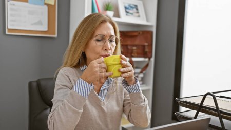 Photo for Mature caucasian woman enjoying coffee in a modern office interior, depicting a professional workplace ambiance. - Royalty Free Image