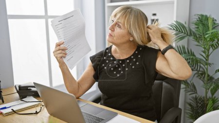 Photo for Charming middle age blonde boss woman, cooling-off at her elegant office using paper documents as a hand fan, multitasking between her laptop business work and beating the indoor heat - Royalty Free Image