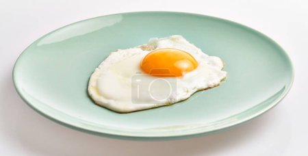 Photo for A sunny-side-up egg served on a pastel green plate isolated on a white background, depicting a simple and healthy breakfast. - Royalty Free Image