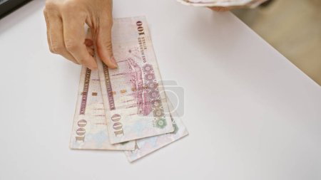 Téléchargez les photos : Les mains d'une femme comptent les billets de banque saoudiens sur un bureau blanc à l'intérieur reflétant la finance et le change. - en image libre de droit