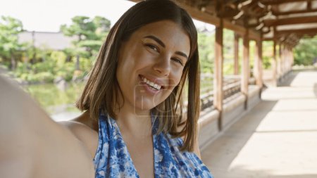 Confident hispanic woman, an all-smile beautiful brunette, enjoys taking a fun selfie at traditional japanese heian jingu shrine, kyoto.