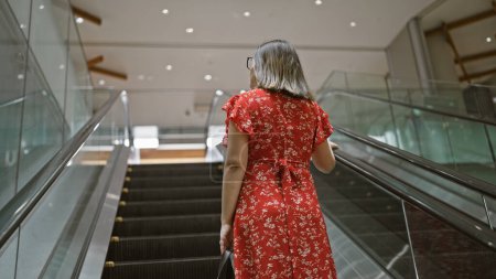 Photo for Stunningly beautiful adult hispanic woman in glasses caught amidst her shopping spree, elegantly ascending the city center's modern escalator - Royalty Free Image