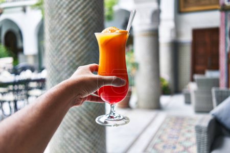 Téléchargez les photos : Homme tenant cocktail coloré à l'extérieur dans un hôtel de luxe, mettant en valeur les loisirs et la détente. - en image libre de droit
