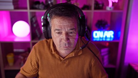 Téléchargez les photos : Un homme mûr avec un casque dans une salle de jeux éclairée au néon la nuit - en image libre de droit