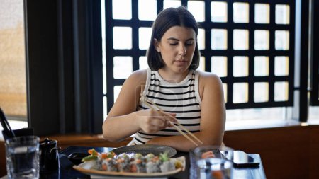 Foto de Joven mujer hispana hermosa comiendo sushi en el restaurante - Imagen libre de derechos