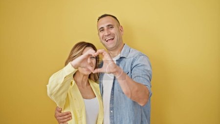 Téléchargez les photos : Homme et femme couple se serrant dans leurs bras en faisant un geste de cœur sur fond jaune isolé - en image libre de droit