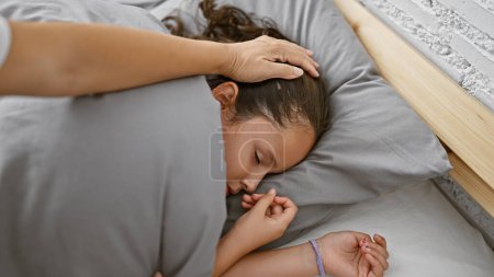 Foto de Madre cariñosa cubriendo a su adormilada hija con una acogedora manta en la comodidad de su dormitorio familiar, disfrutando de un momento de relax juntos antes de acostarse - Imagen libre de derechos