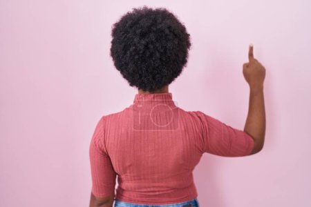 Photo for Beautiful african woman with curly hair standing over pink background posing backwards pointing ahead with finger hand - Royalty Free Image
