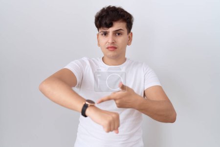 Téléchargez les photos : Jeune homme non binaire portant casual t-shirt blanc à la hâte pointant vers regarder le temps, l'impatience, bouleversé et en colère pour retard de délai - en image libre de droit