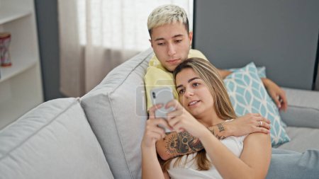 Téléchargez les photos : Beau couple utilisant smartphone souriant à la maison - en image libre de droit