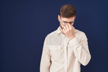 Foto de Hombre hispano con barba de pie sobre fondo azul cansado frotando nariz y ojos sintiendo fatiga y dolor de cabeza. concepto de estrés y frustración. - Imagen libre de derechos
