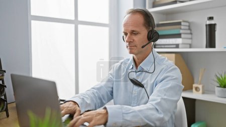 Photo for Mature, handsome hispanic business man, working hard at the office. using his laptop, sporting headphones, concentrating on a serious video call conference. - Royalty Free Image