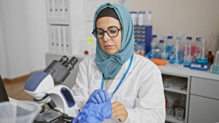 Photo for Mature woman scientist with headscarf working in laboratory using microscope - Royalty Free Image