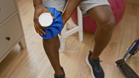 Téléchargez les photos : Un homme afro-américain applique de la glace au genou dans une clinique de désintox, dépeignant la guérison et les soins de santé. - en image libre de droit