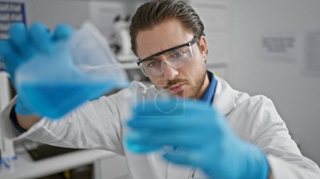 Photo for Young hispanic man scientist pouring liquid on glass at laboratory - Royalty Free Image